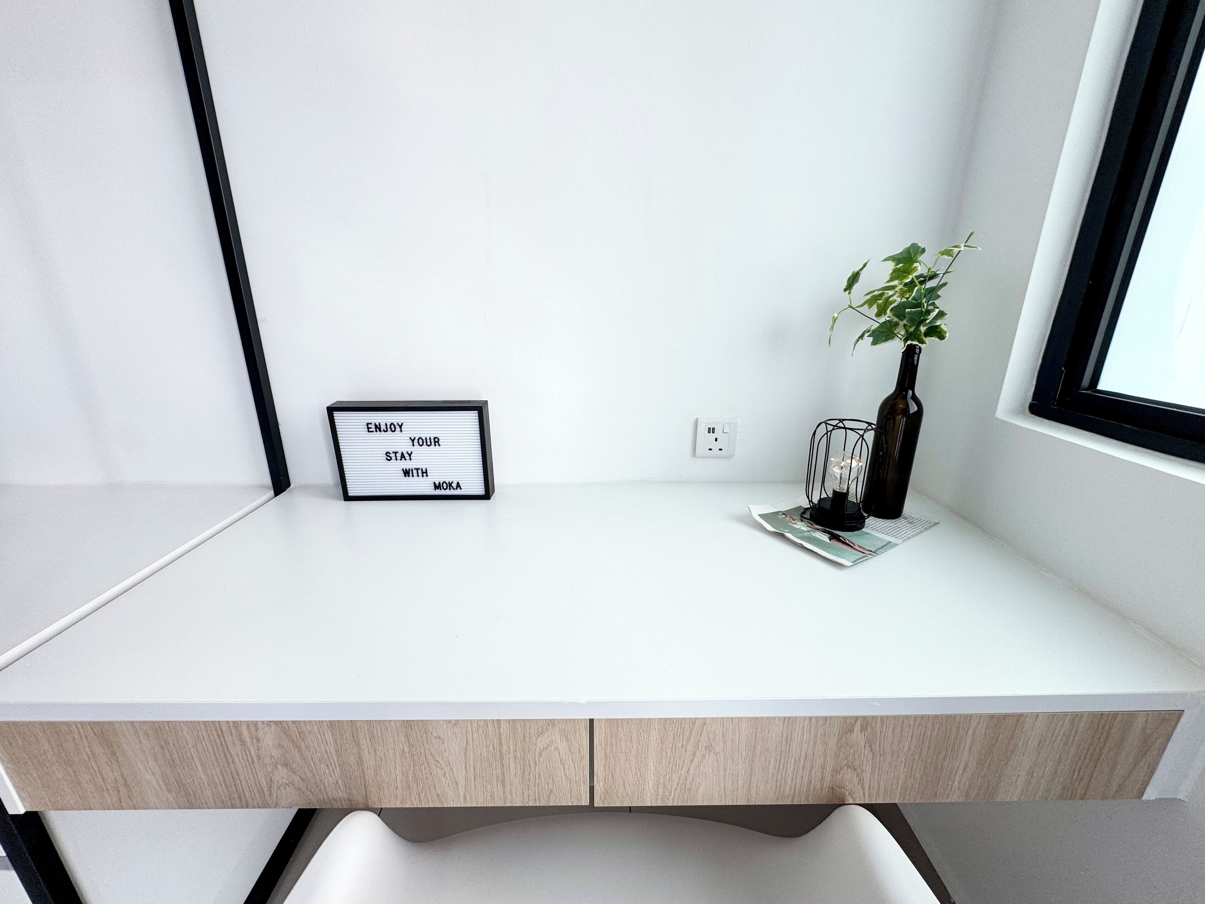 Uma mesa branca com um quadro de avisos, uma planta e uma garrafa.