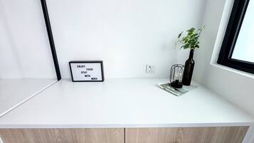 Uma mesa branca com um quadro de avisos, uma planta e uma garrafa.