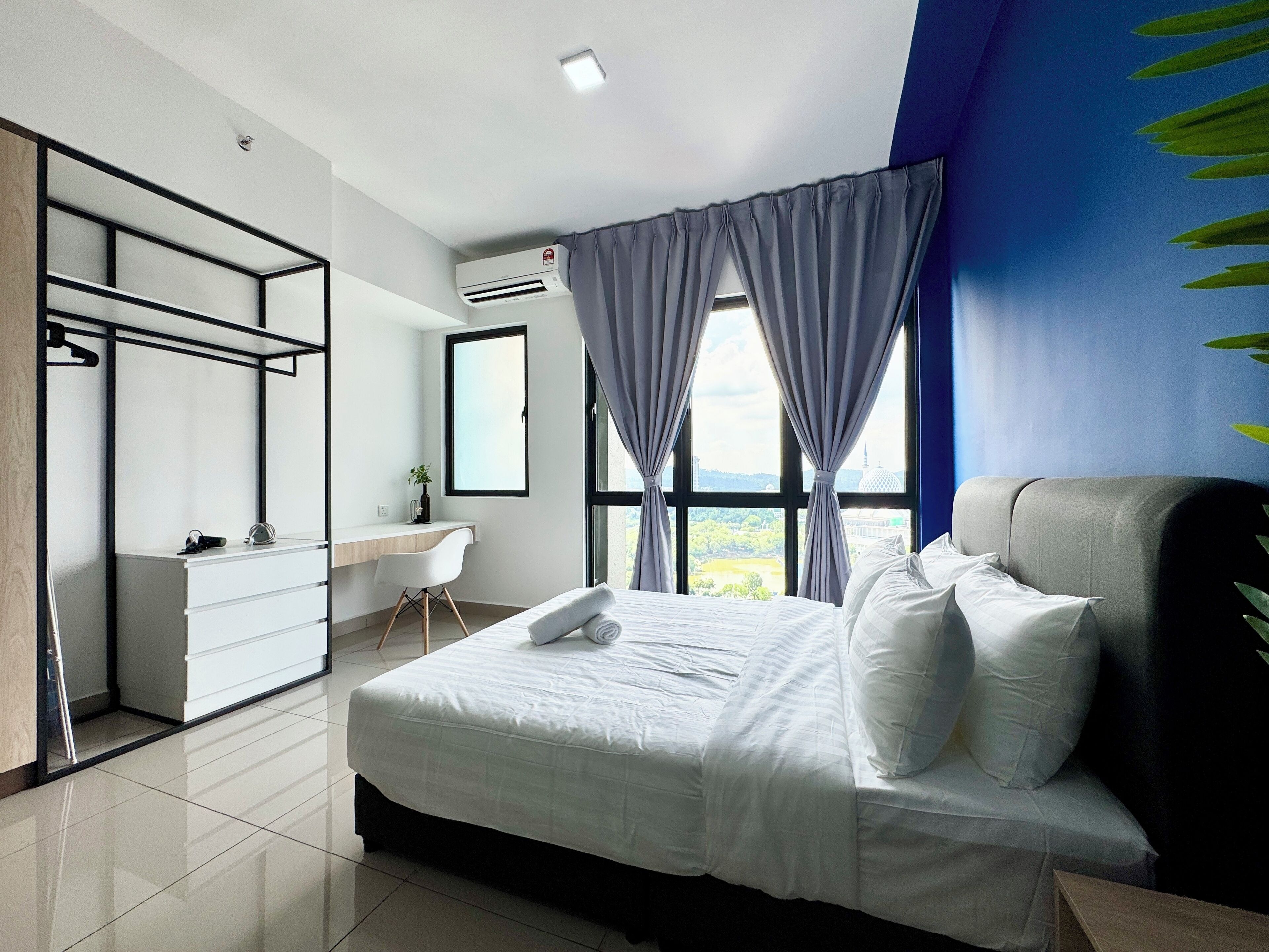 A modern hotel room with a large bed, a desk, and a wardrobe.