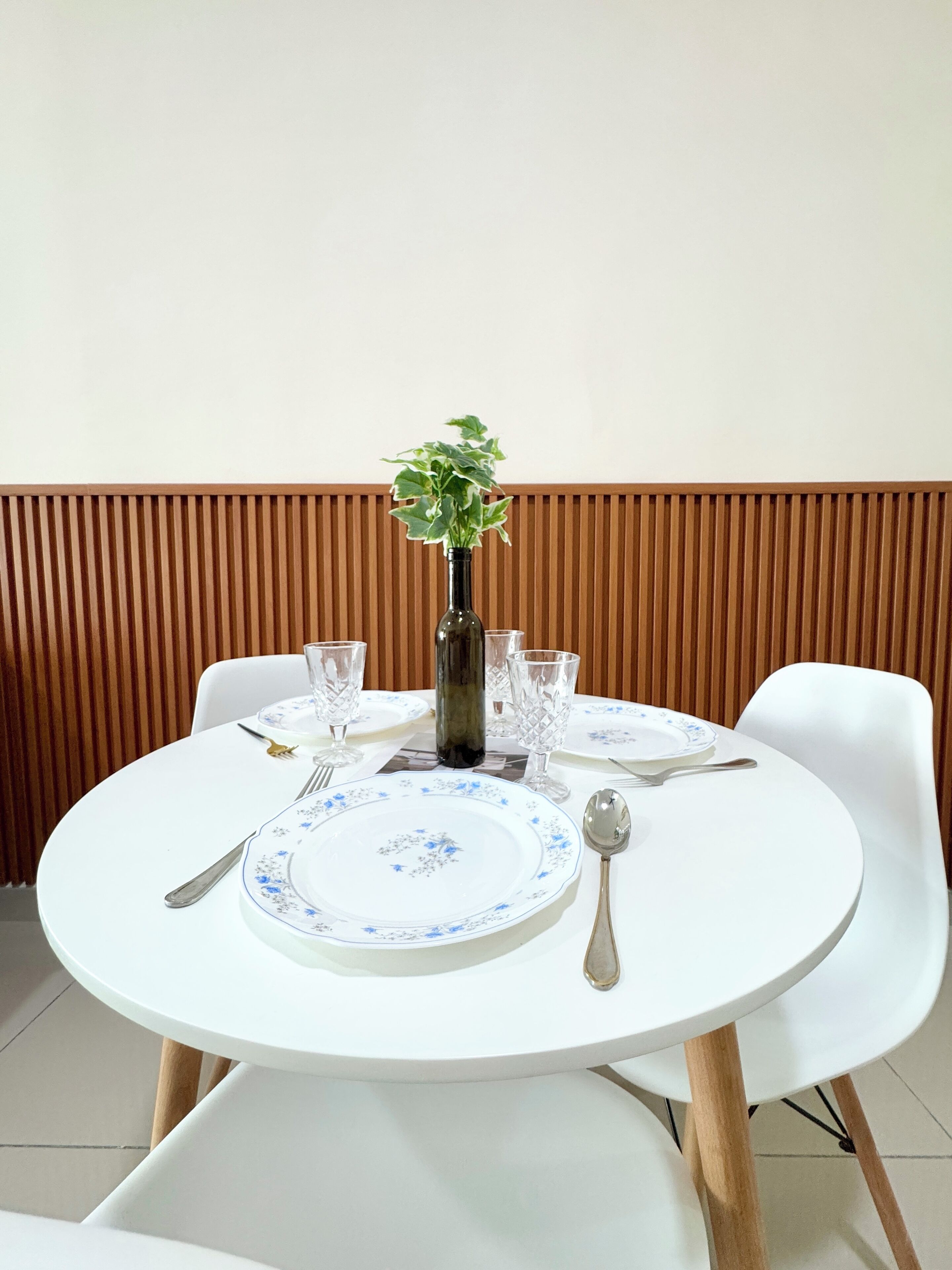 A round dining table with white chairs, a vase with green plants, and a plate with blue floral patterns.
