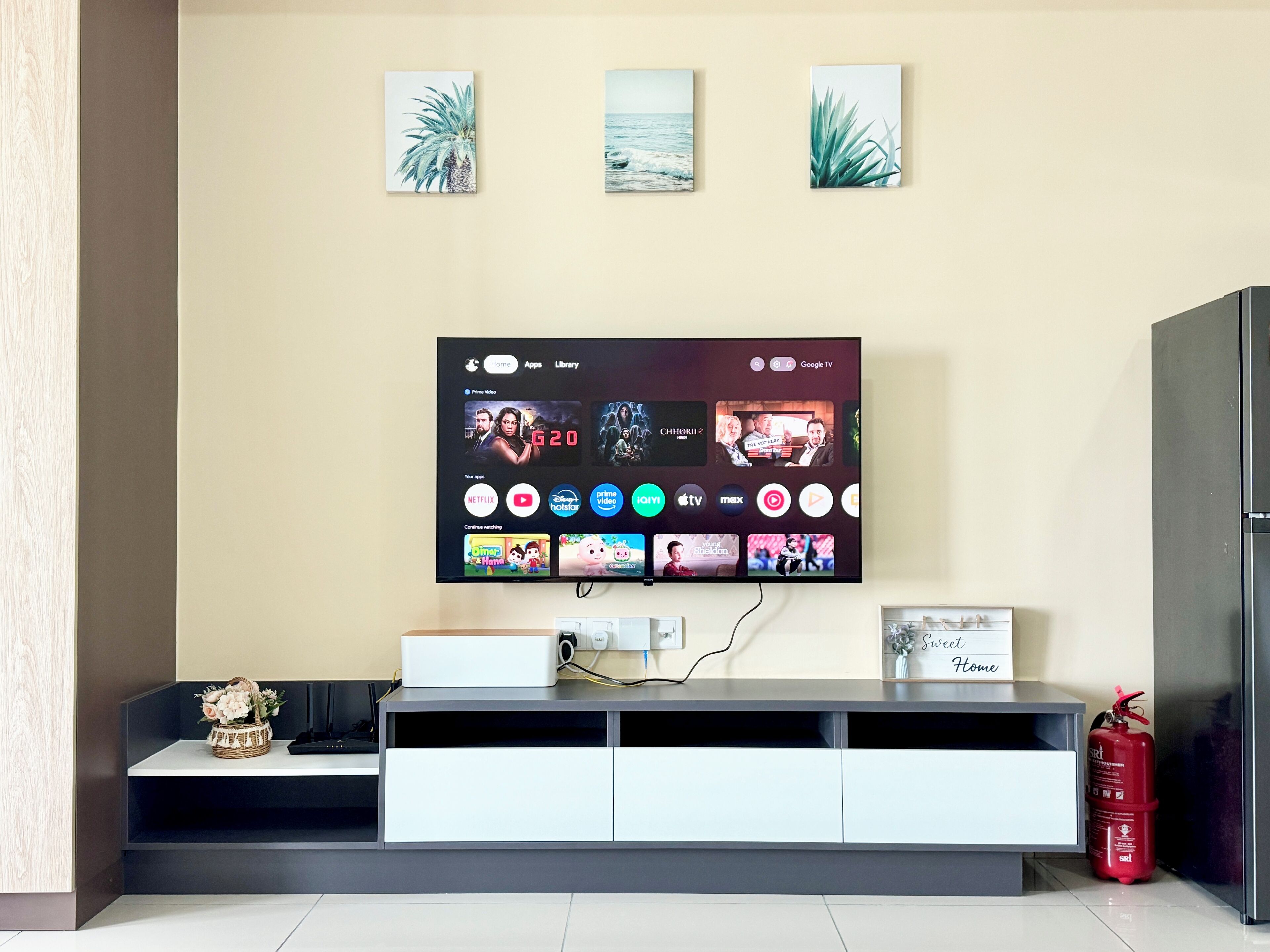 A modern living room with a flat-screen TV mounted on the wall, a white entertainment unit below, and a fire extinguisher on the floor.