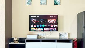 A modern living room with a flat-screen TV mounted on the wall, a white entertainment unit below, and a fire extinguisher on the floor.