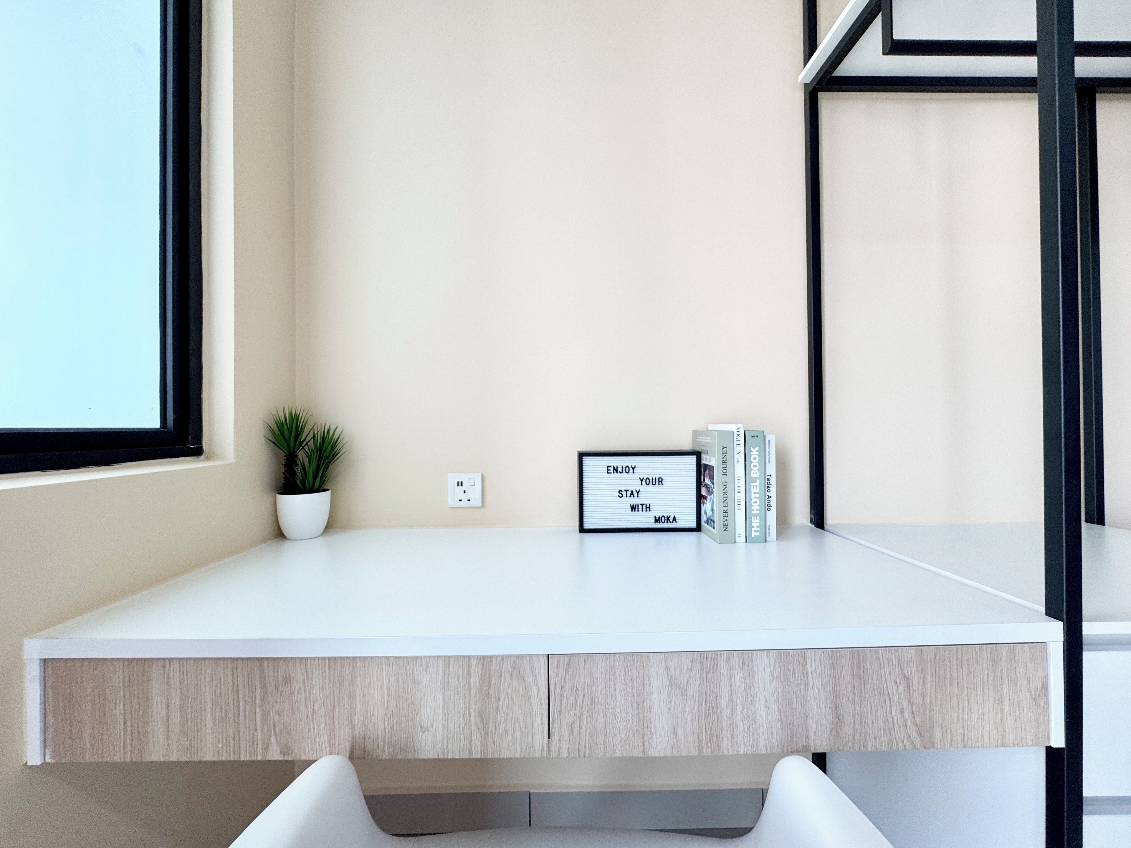 A modern desk with a light wood finish, a potted plant, a motivational sign, and a stack of books.