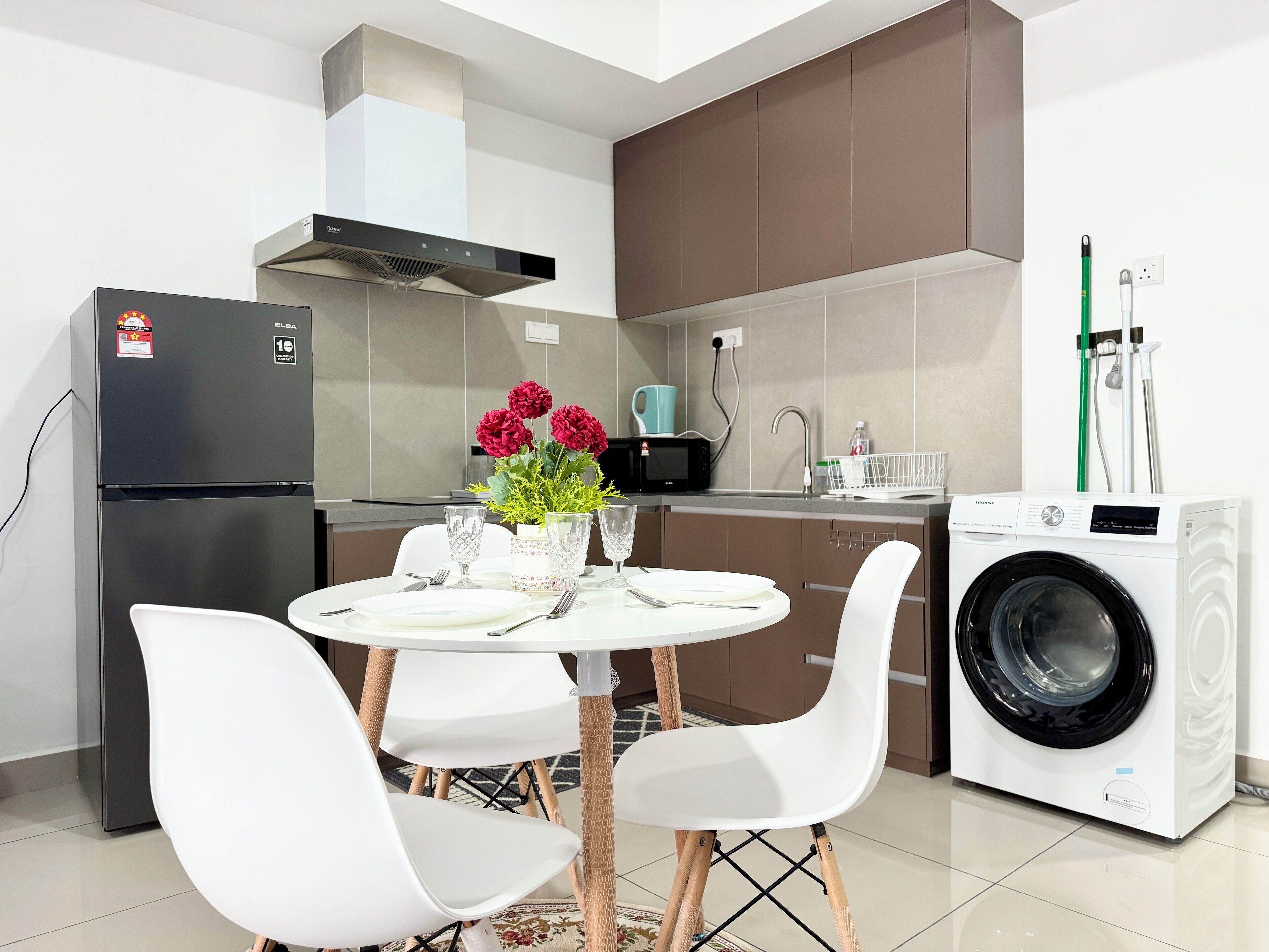 A modern kitchen with a refrigerator, microwave, washing machine, and a dining table with chairs.