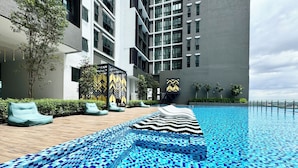 A modern hotel with a swimming pool featuring blue mosaic tiles, outdoor seating, and a view of the city skyline. - Alinea Suites (Shah Alam)