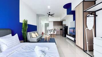 A modern hotel room with a large bed, a seating area with a sofa and chairs, a kitchenette, and a television.