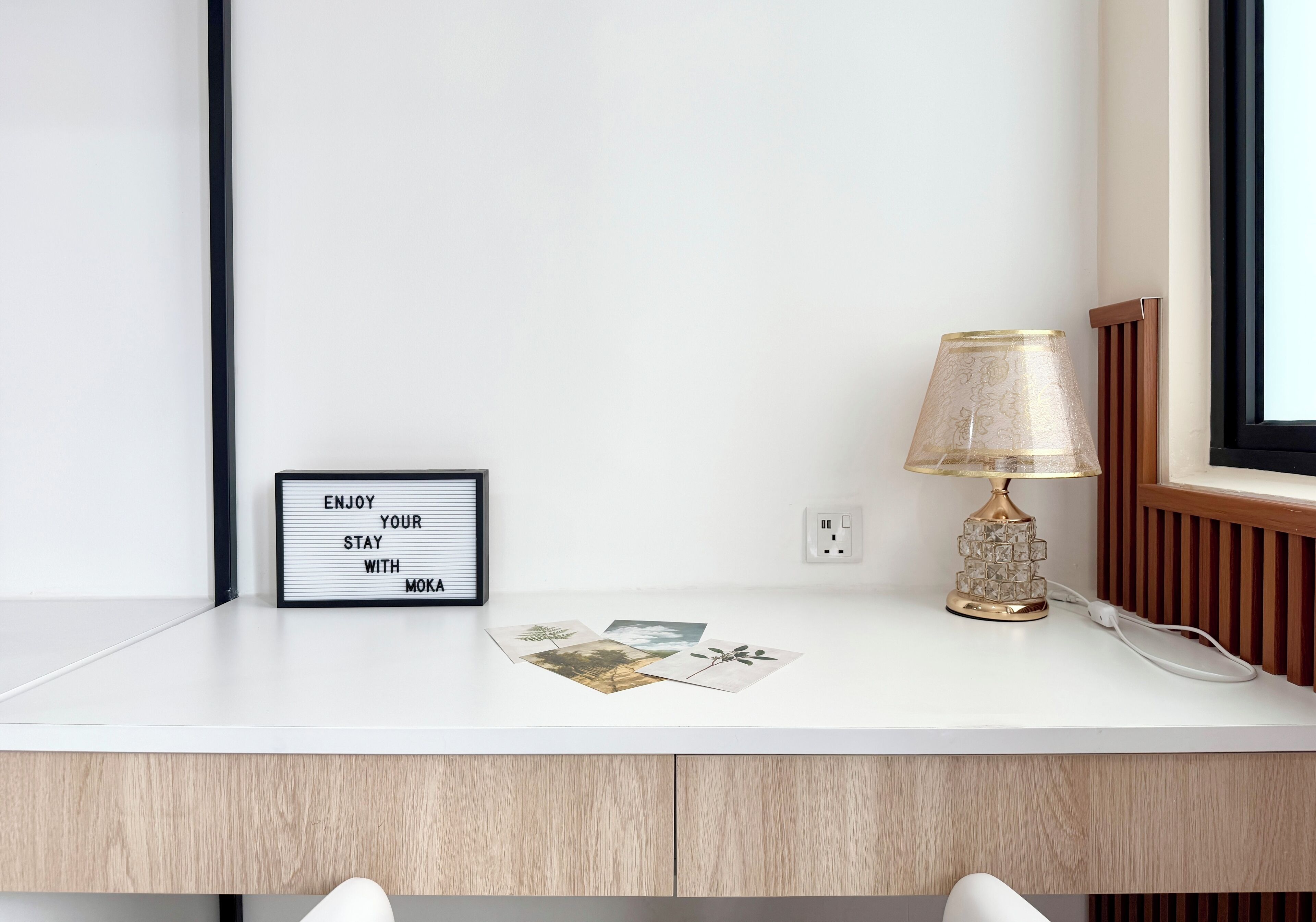 Et hvidt skrivebord med et indrammet skilt, en lampe og nogle billeder.
