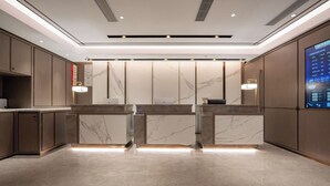 A modern hotel lobby with marble reception counters, recessed lighting, and a digital display on the right wall. - World Hotel (Jinan CBD Dingjiazhuang Subway Station) (Jinan)