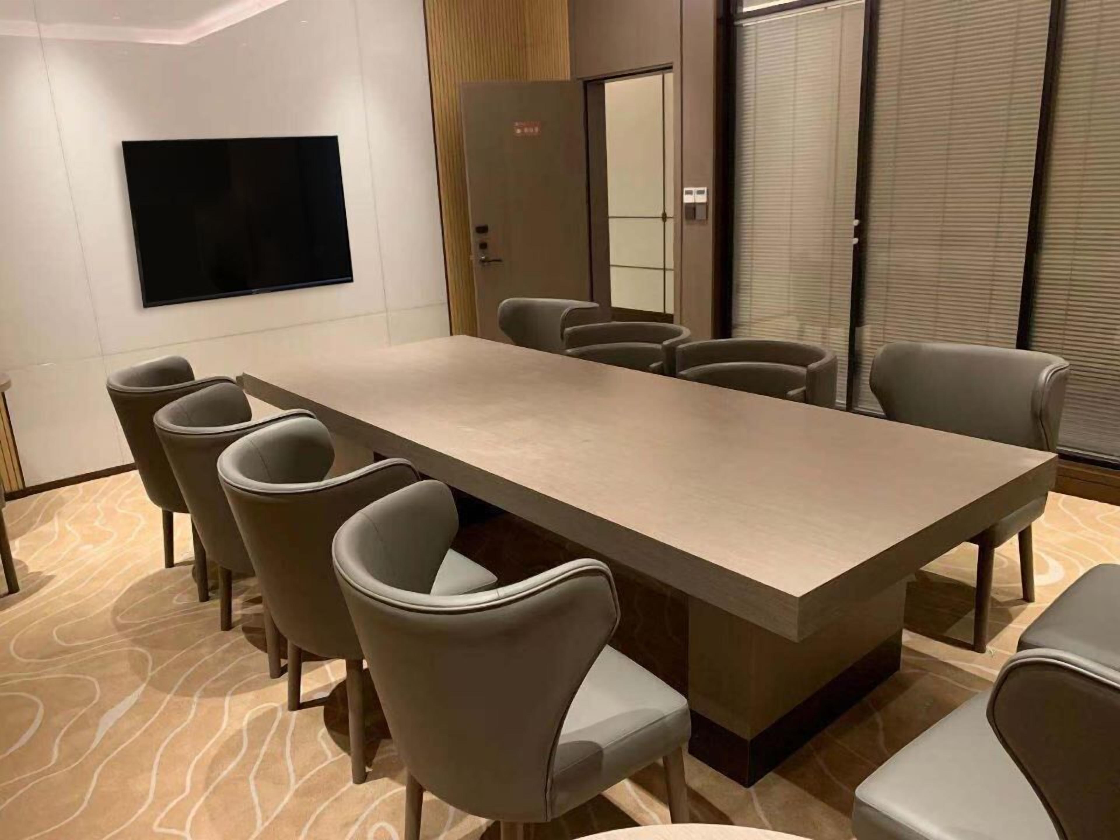 A conference room with a long table, six chairs, a flat-screen TV, and a door with a security panel.