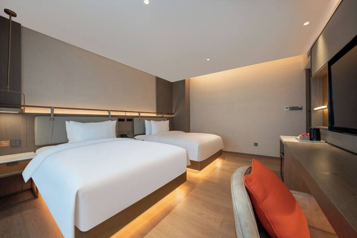 A modern hotel room with two beds, a flat-screen TV, and a wooden floor.