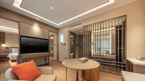 A modern hotel room with a flat-screen TV, a round table, a sofa with an orange pillow, and a sliding glass door leading to a balcony. - World Hotel (Jinan CBD Dingjiazhuang Subway Station) (Jinan)