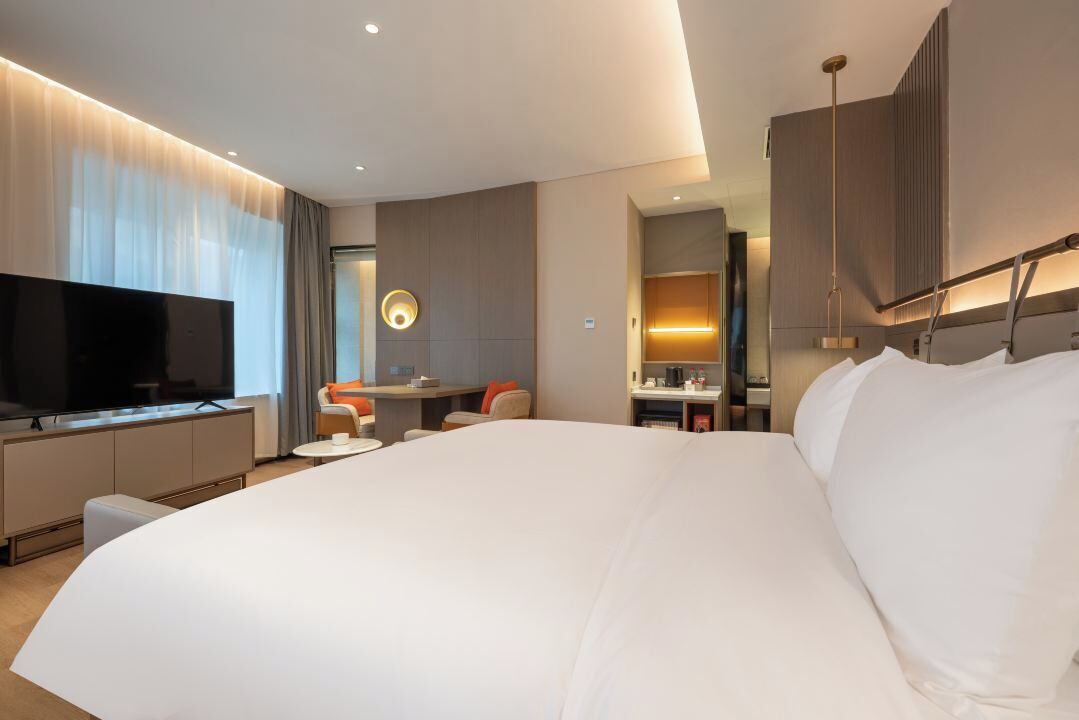 A modern hotel room with a large bed, a flat-screen TV, a desk, and a bathroom.
