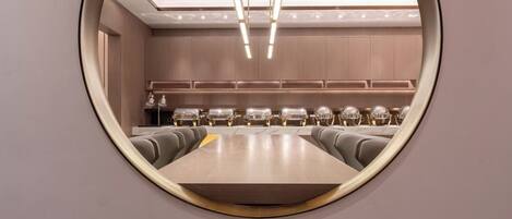 A modern conference room with a round table, grey upholstered chairs, and a central chandelier.