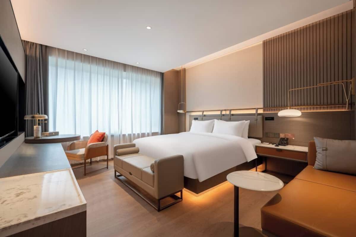 A modern hotel room with a large bed, a desk, a chair, and a small table.