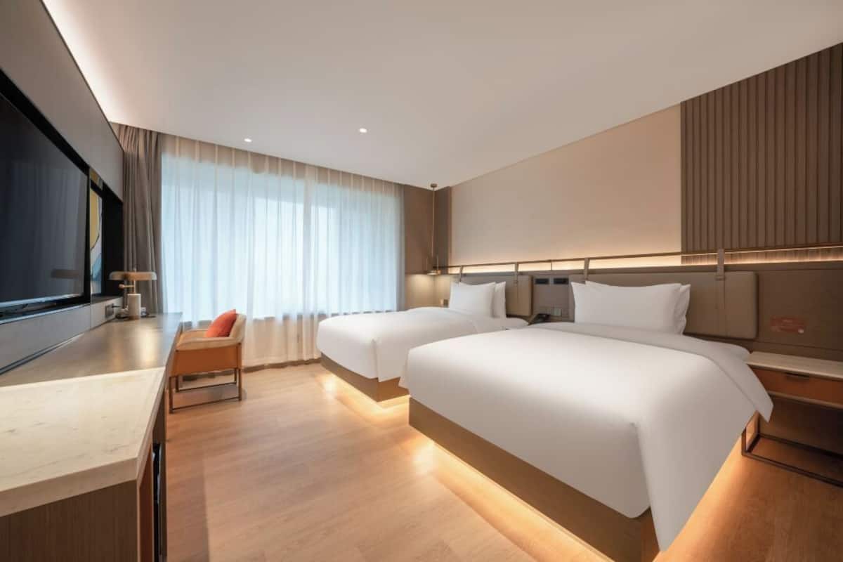 A modern hotel room with two beds, a desk, and a large window with curtains.