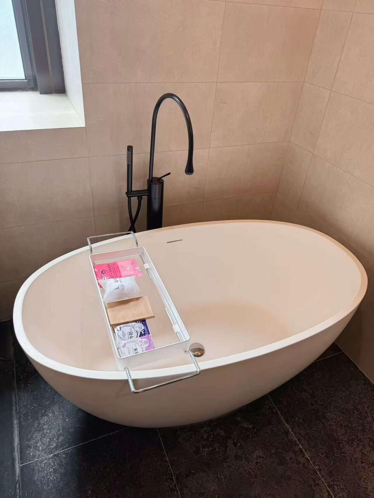 A modern bathroom with a freestanding bathtub, a towel rack, and a window providing natural light.