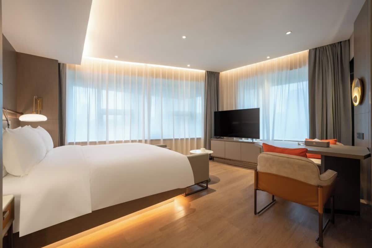 A modern hotel room with a large bed, a desk with a flat-screen TV, and a seating area.