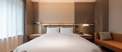 Ein modernes Hotelzimmer mit einem großen Bett, Nachttischen, einer Couch und einem großen Fenster mit Vorhängen.