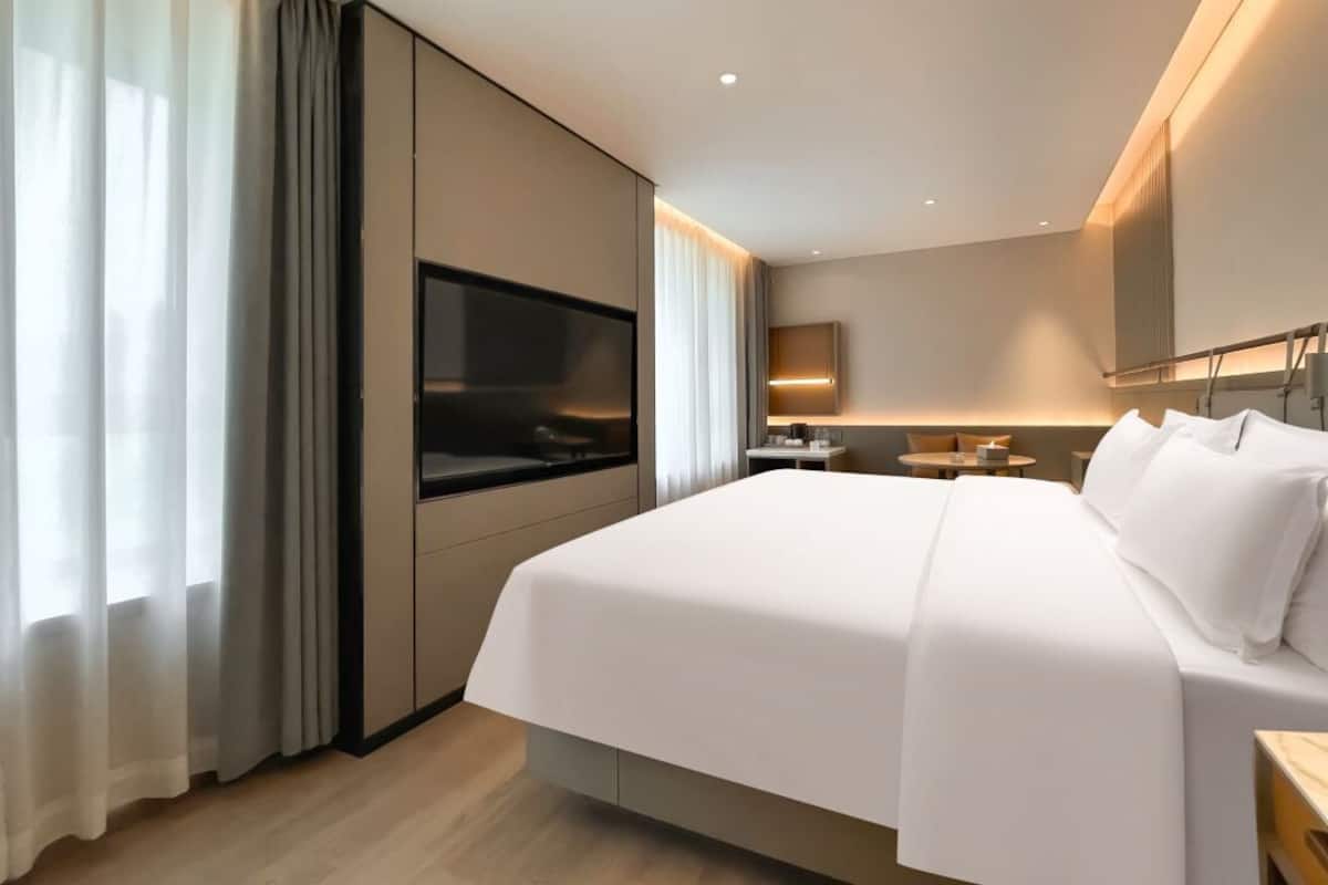 A modern hotel room with a large bed, a flat-screen TV, a desk, and a small seating area.
