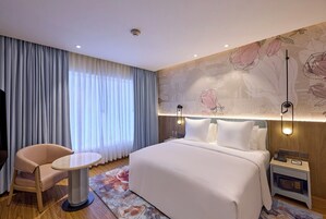 A modern hotel room with a large bed, a desk, and a chair.