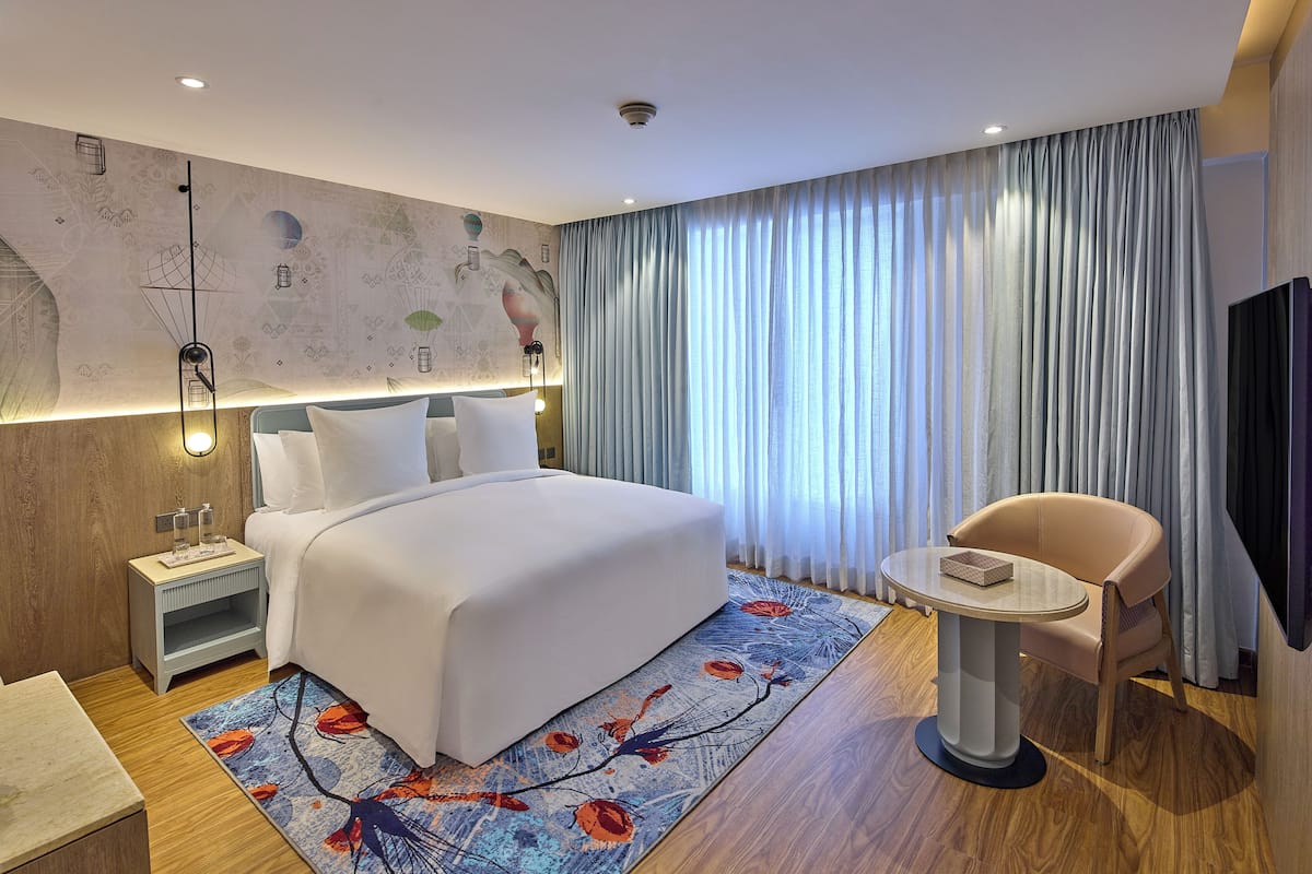A modern hotel room with a large bed, a side table, a chair, and a television.