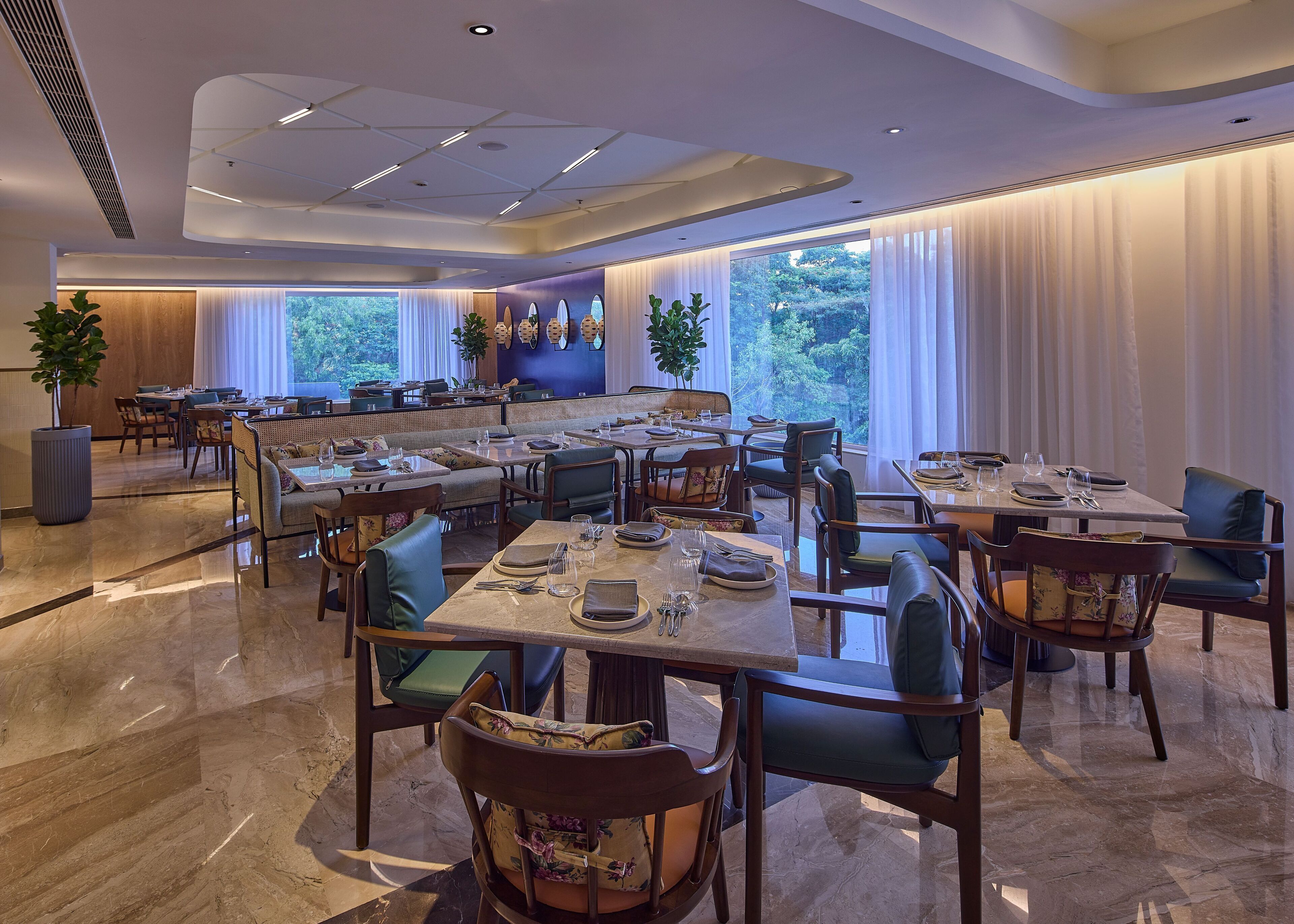 A spacious dining area with multiple tables and chairs, large windows with curtains, and a modern ceiling design.