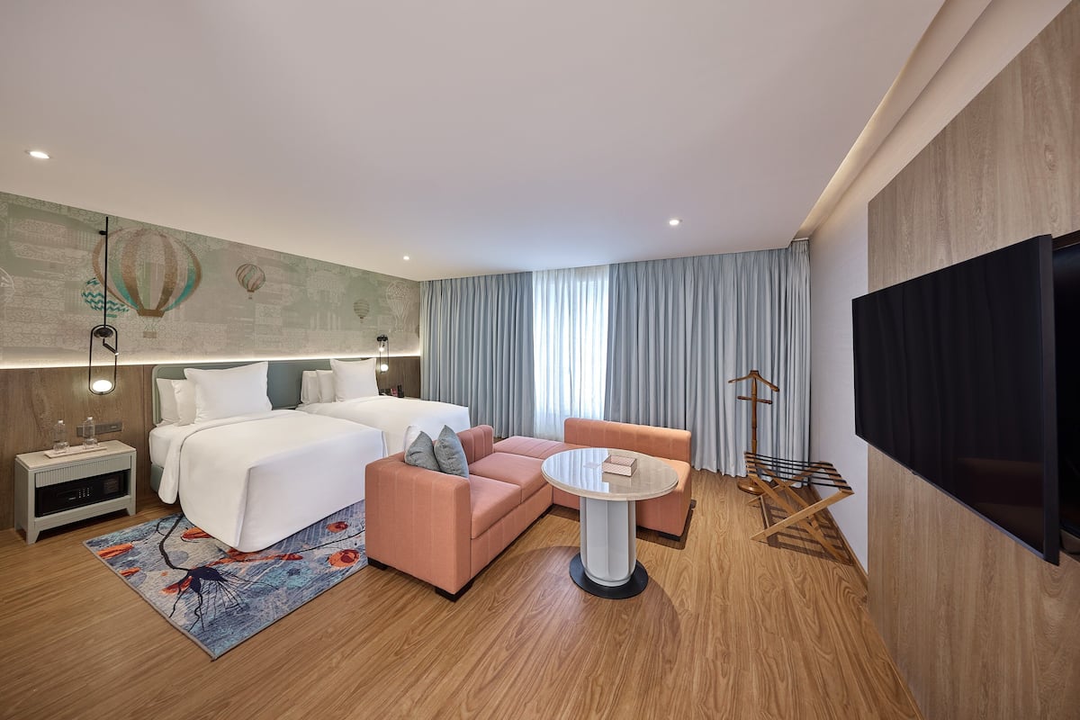A modern hotel room with a bed, a pink sofa, a round table, and a TV.