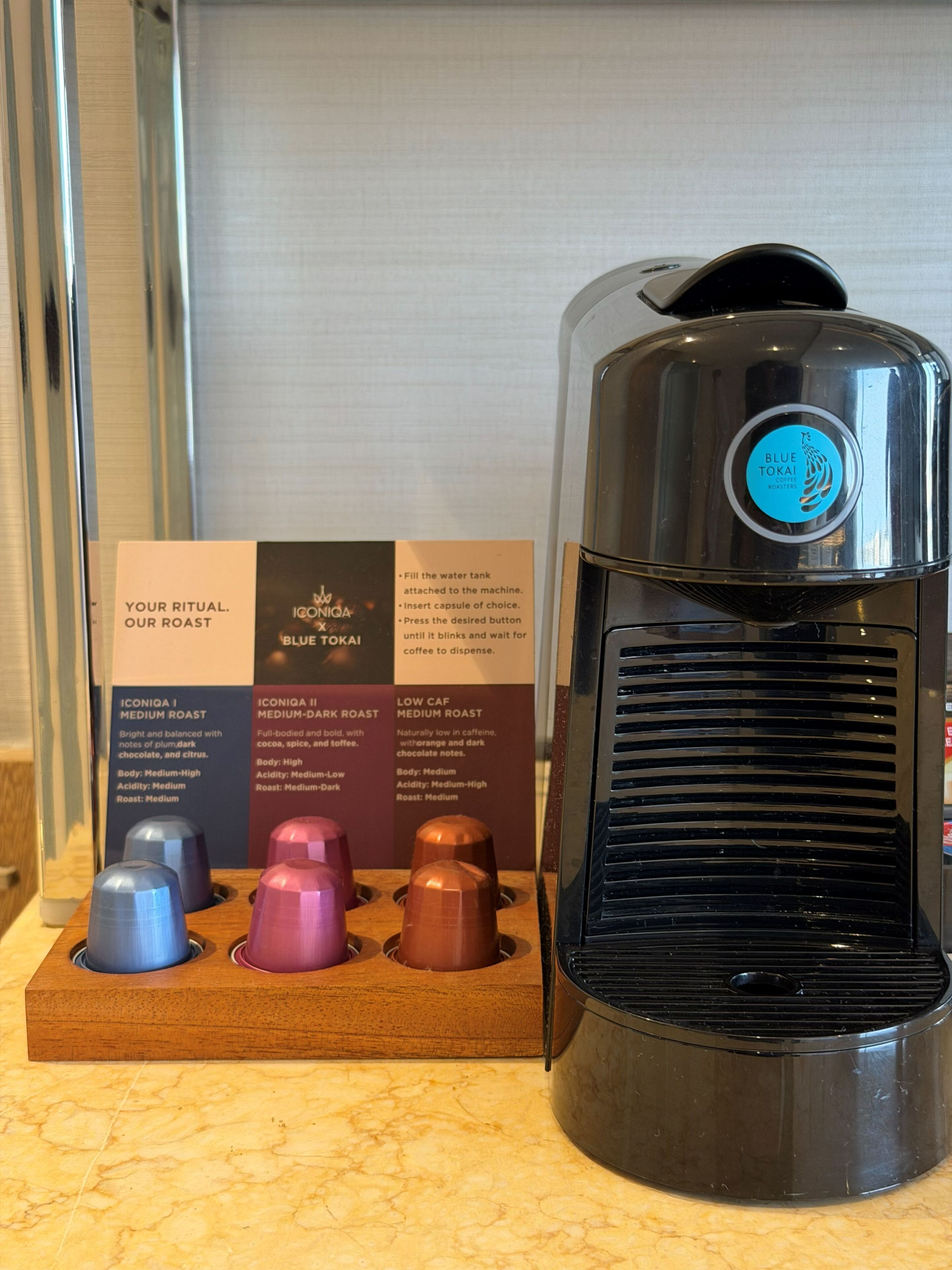 Une machine à café avec un logo bleu, un compartiment pour les dosettes de café contenant trois dosettes, et un panneau indiquant les différentes options de torréfaction du café.