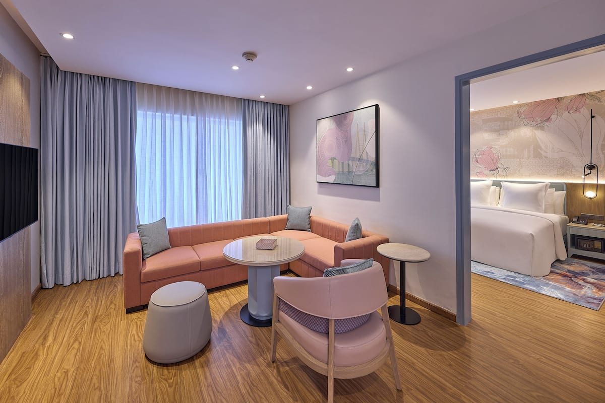A modern hotel room with a sofa, ottoman, chair, and a small table.