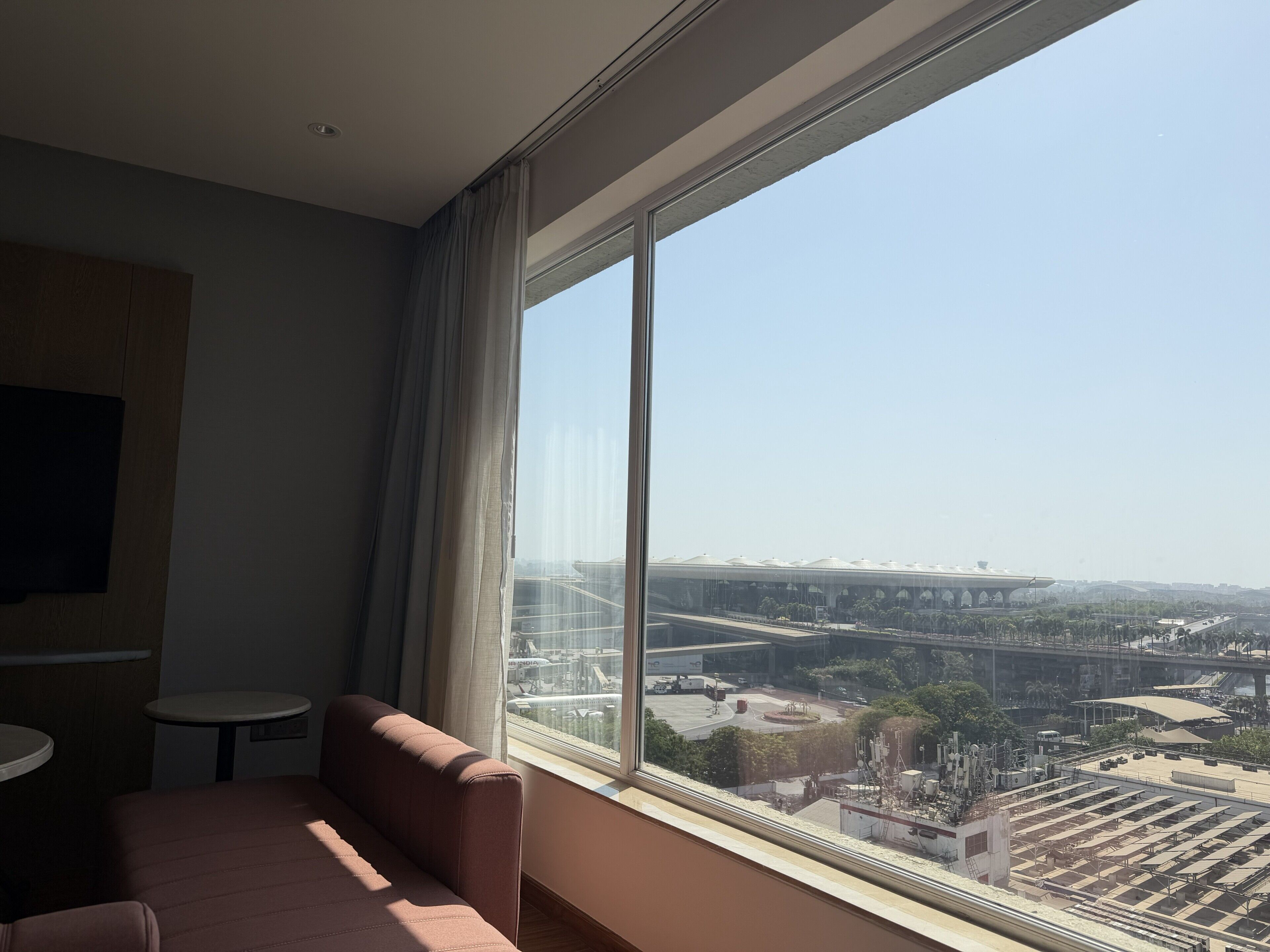 A room with a large window, a sofa, a small table, and a flat-screen TV.