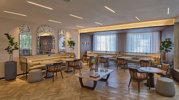 Amplia sala de estar con piso de madera en patrón de espiga, una mesa de centro, diversas opciones de asientos que incluyen sofás y sillones, y ventanas grandes que proporcionan luz natural.