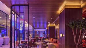 A modern hotel lobby with a seating area, a reception desk, and a large potted plant.