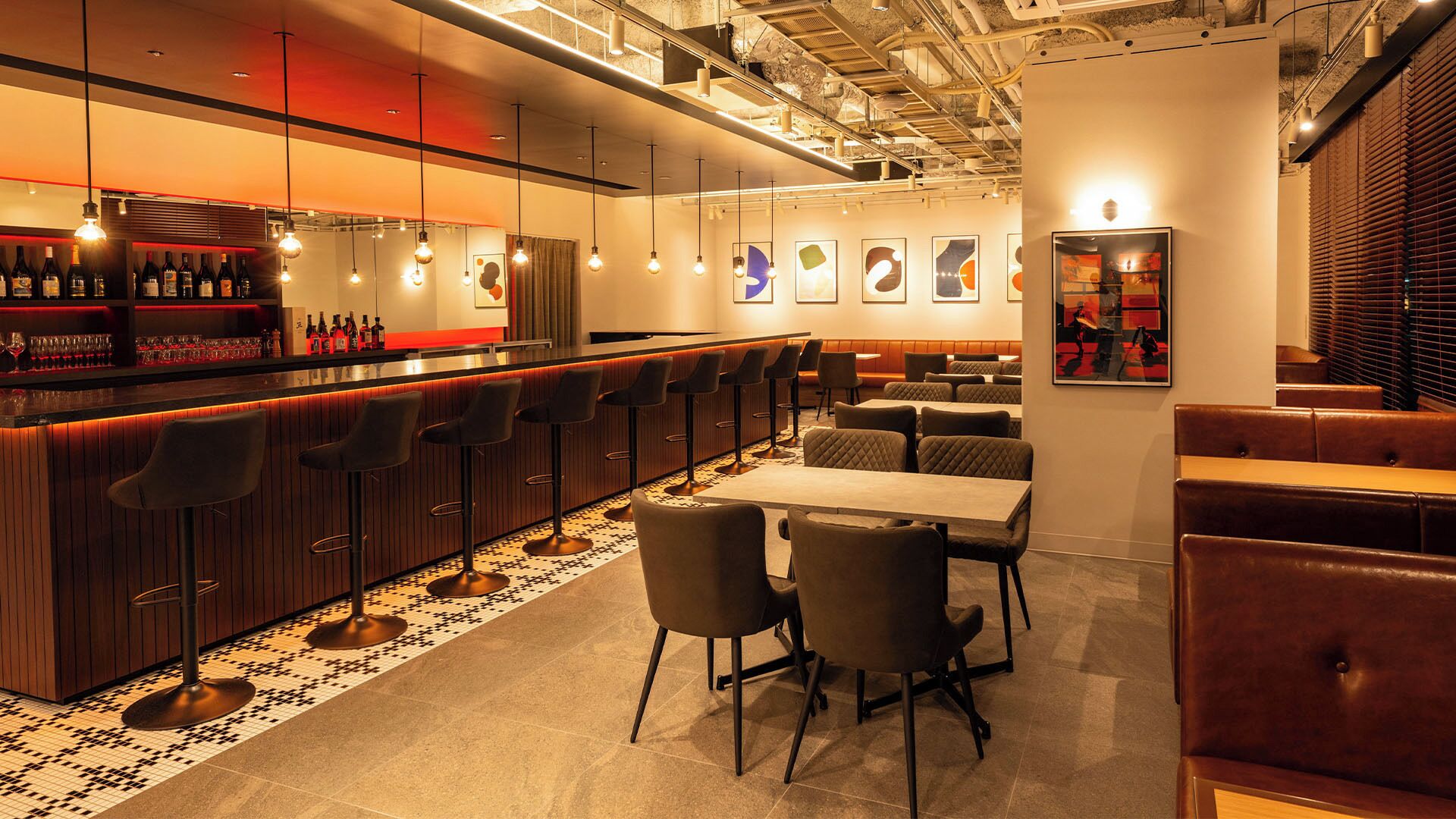 A modern bar area with a long counter, multiple stools, and a seating area with tables and chairs.