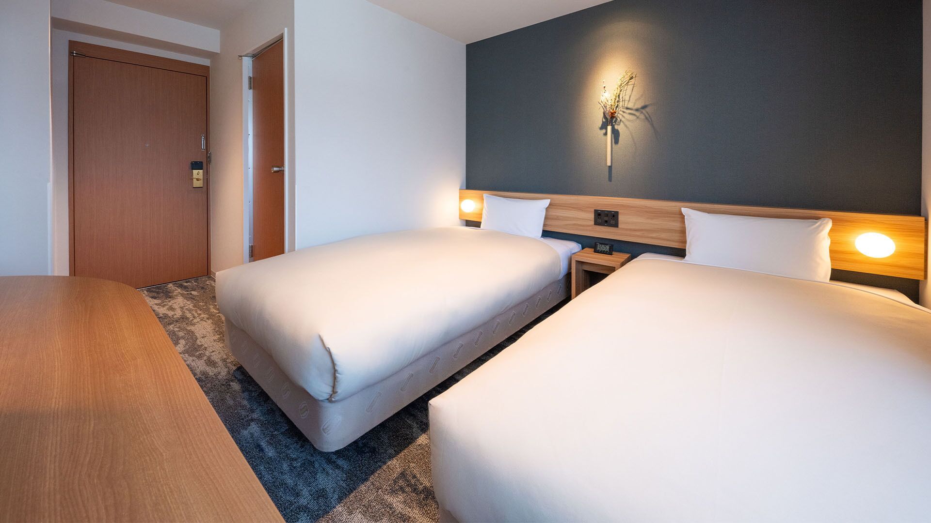 Una camera d'albergo con due letti, una testiera in legno, un lampadario a parete e una porta.
