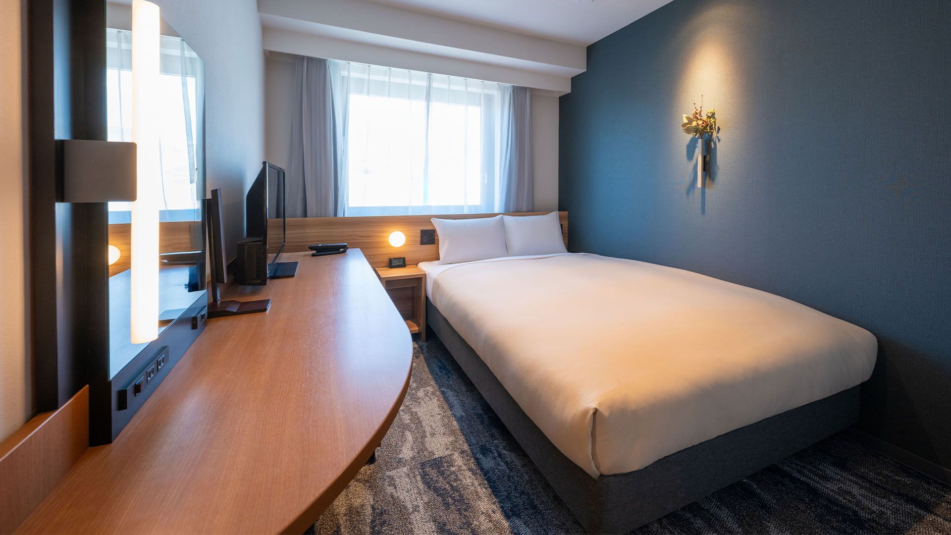 Una camera d'albergo con un letto, una scrivania, una televisione e una finestra con tende.