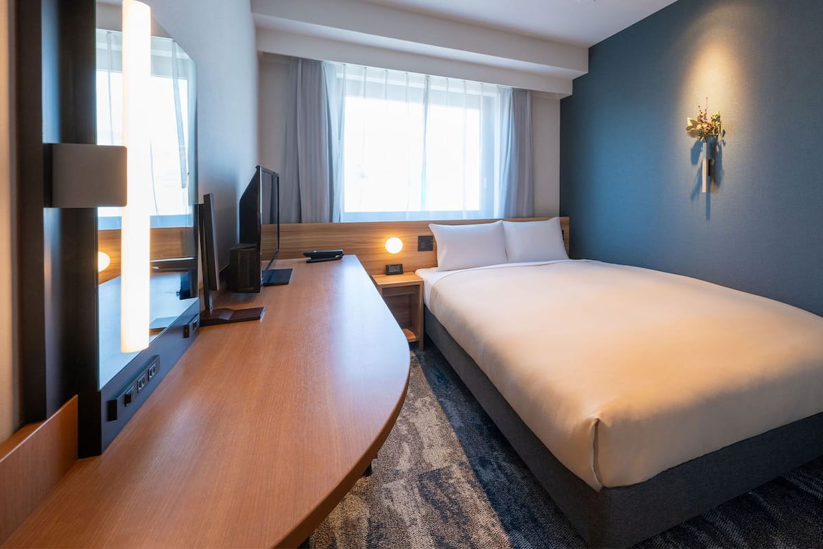 Ein Hotelzimmer mit Bett, Schreibtisch, Fernseher und einem Fenster mit Vorhängen.
