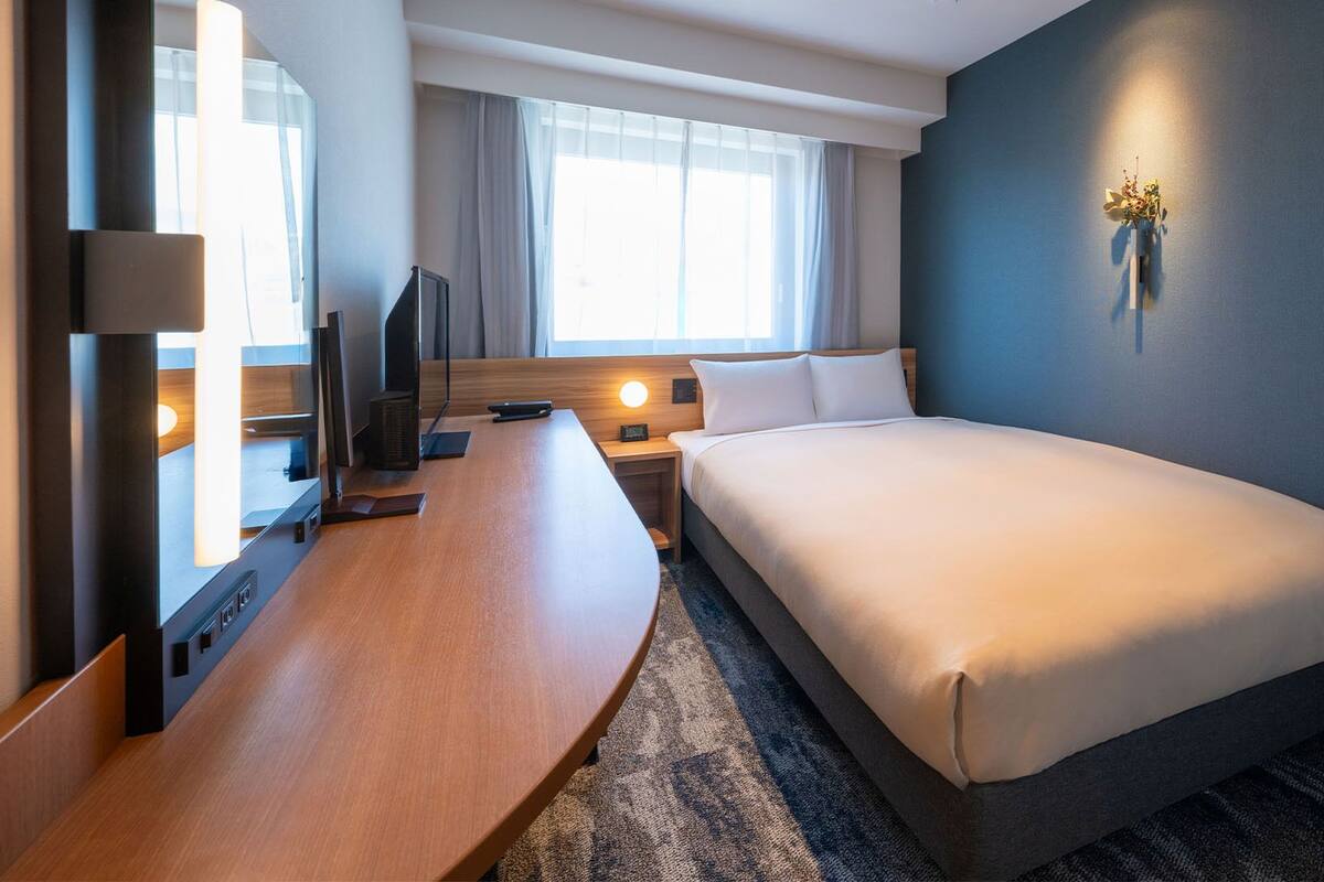 A hotel room with a bed, a desk, a TV, and a window with curtains.