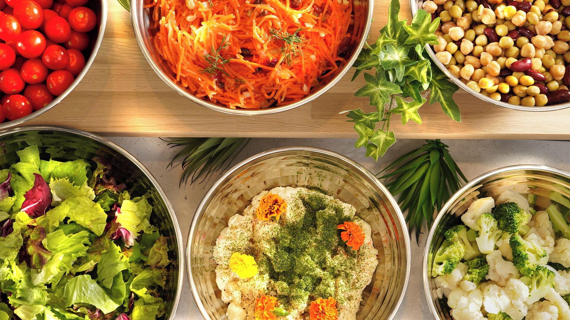 A variety of dishes including a salad with lettuce, a carrot salad, chickpeas, and a bowl with cauliflower and broccoli.