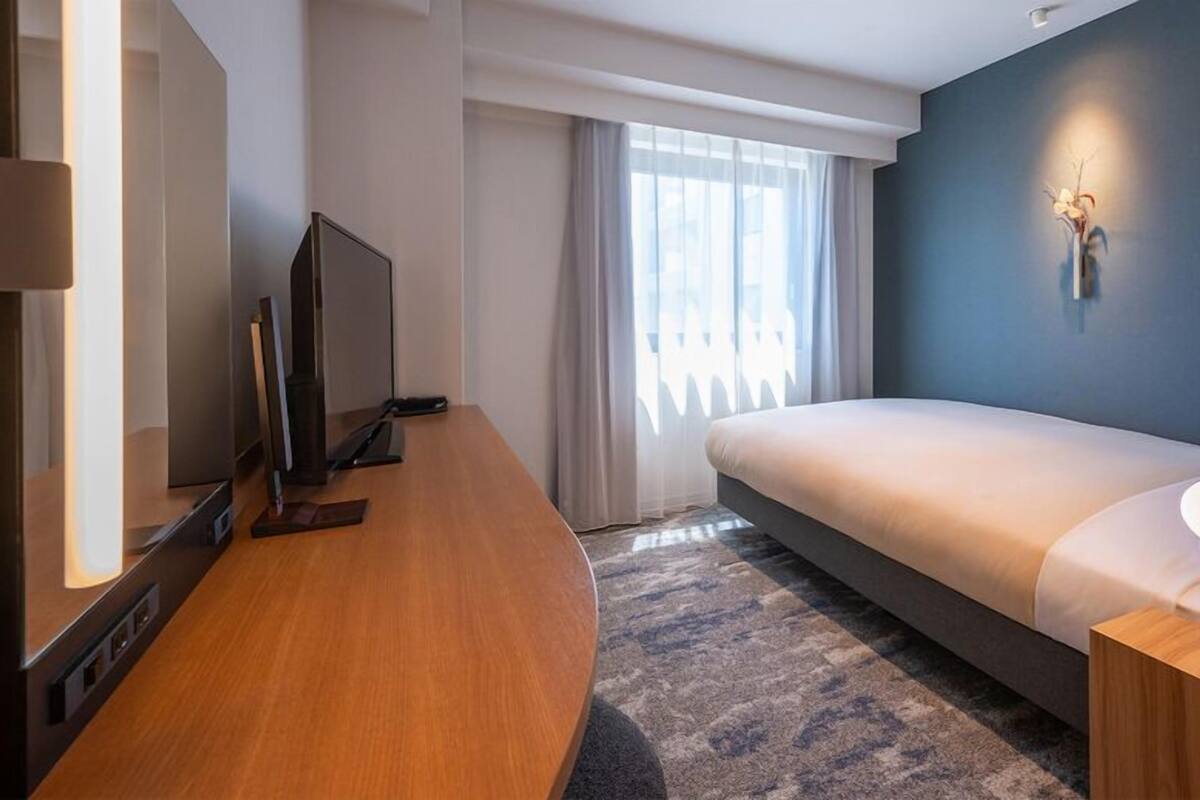 Ein modernes Hotelzimmer mit einem Bett, einem Schreibtisch, einem Fernseher und einer Wandleuchte.