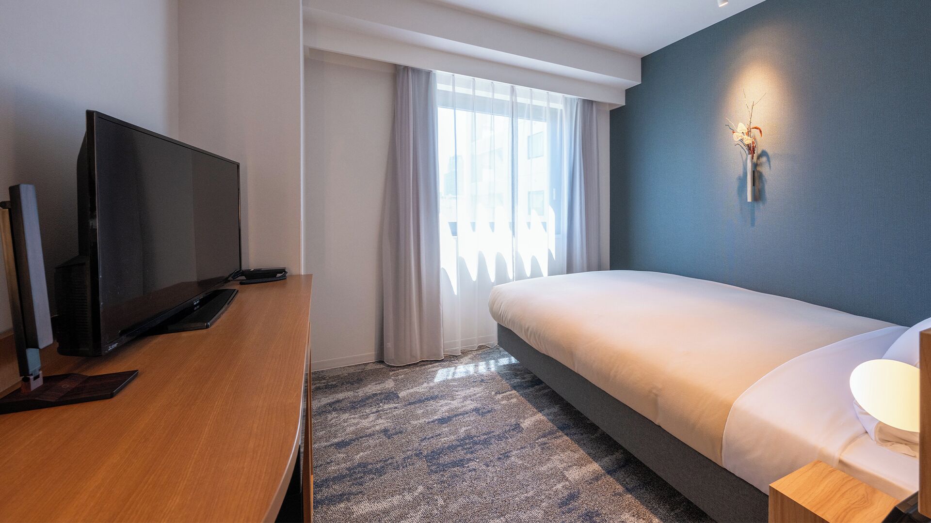 Ein modernes Hotelzimmer mit einem Bett, einem Schreibtisch mit Fernseher und einem Vorhangfenster.