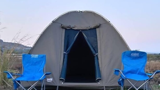 Een tent met twee blauwe opklapstoelen ervoor.