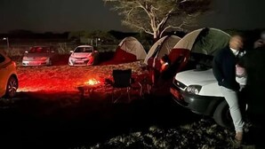 Een camping in de nacht met tenten, een auto en een kampvuur.