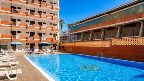 A hotel with a swimming pool, sun loungers, and a multi-story building with balconies.