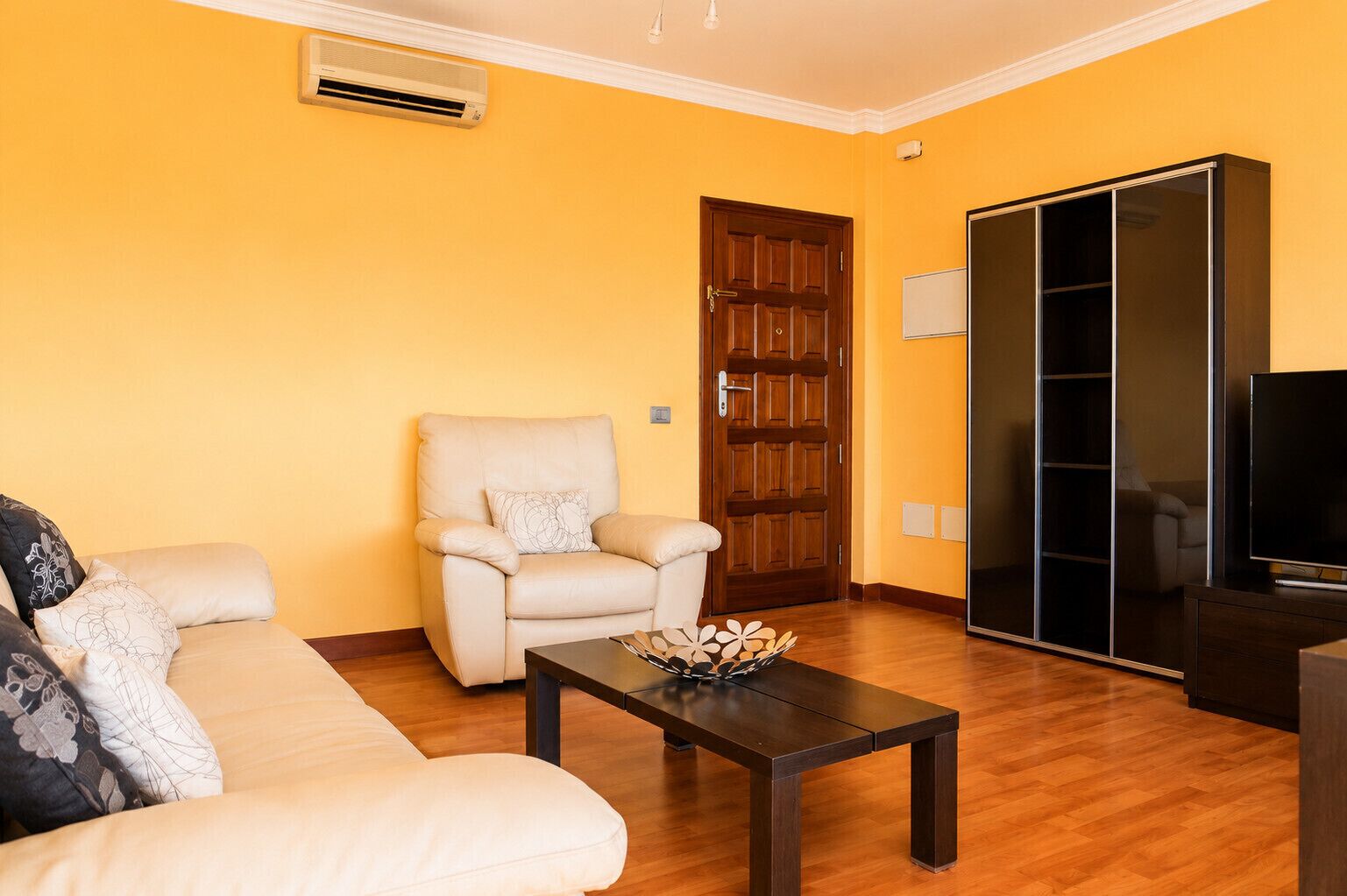 Un salon comprenant un canapé, un fauteuil, une table basse, un téléviseur et un placard avec une porte coulissante.