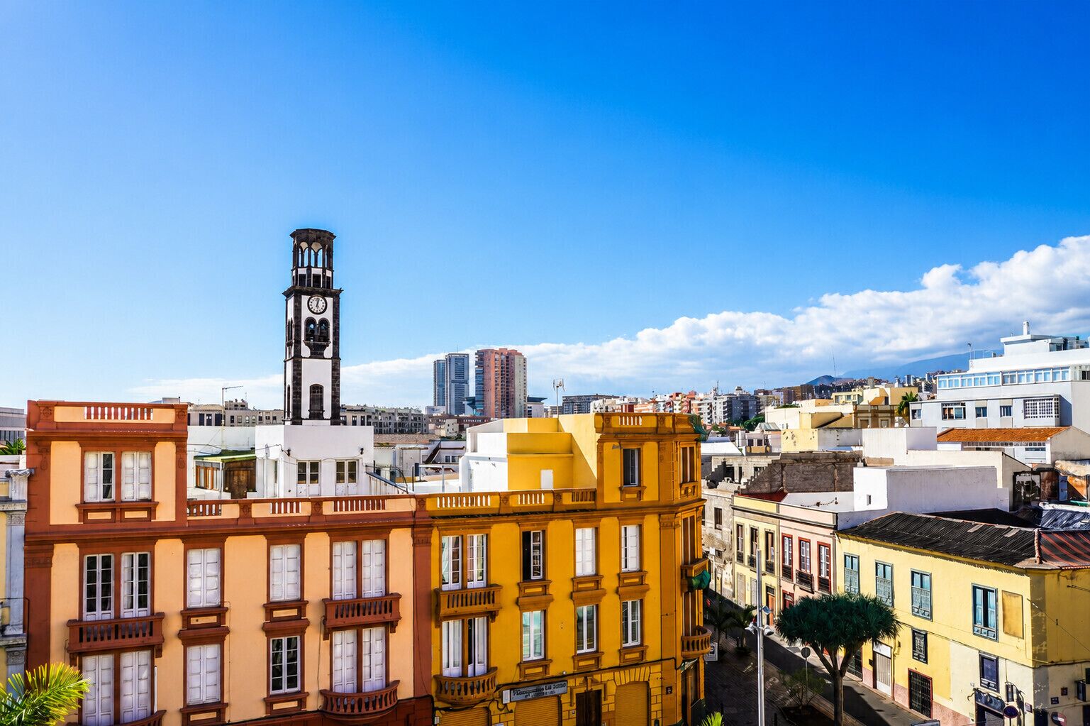 Un paisaje urbano con una imponente torre de reloj, edificios de colores y un cielo azul despejado.