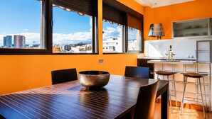 A modern kitchen with a dining area, large windows, and a view of the cityscape.