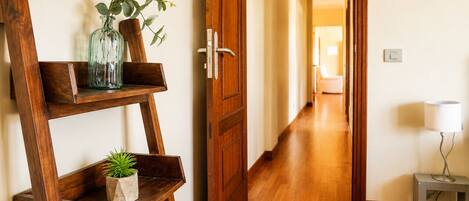 Un interior de madera con un pasillo, una puerta, una mesita con una lámpara y una estantería con plantas.