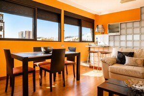 A modern living room with a dining area, large windows, and a view of the cityscape.