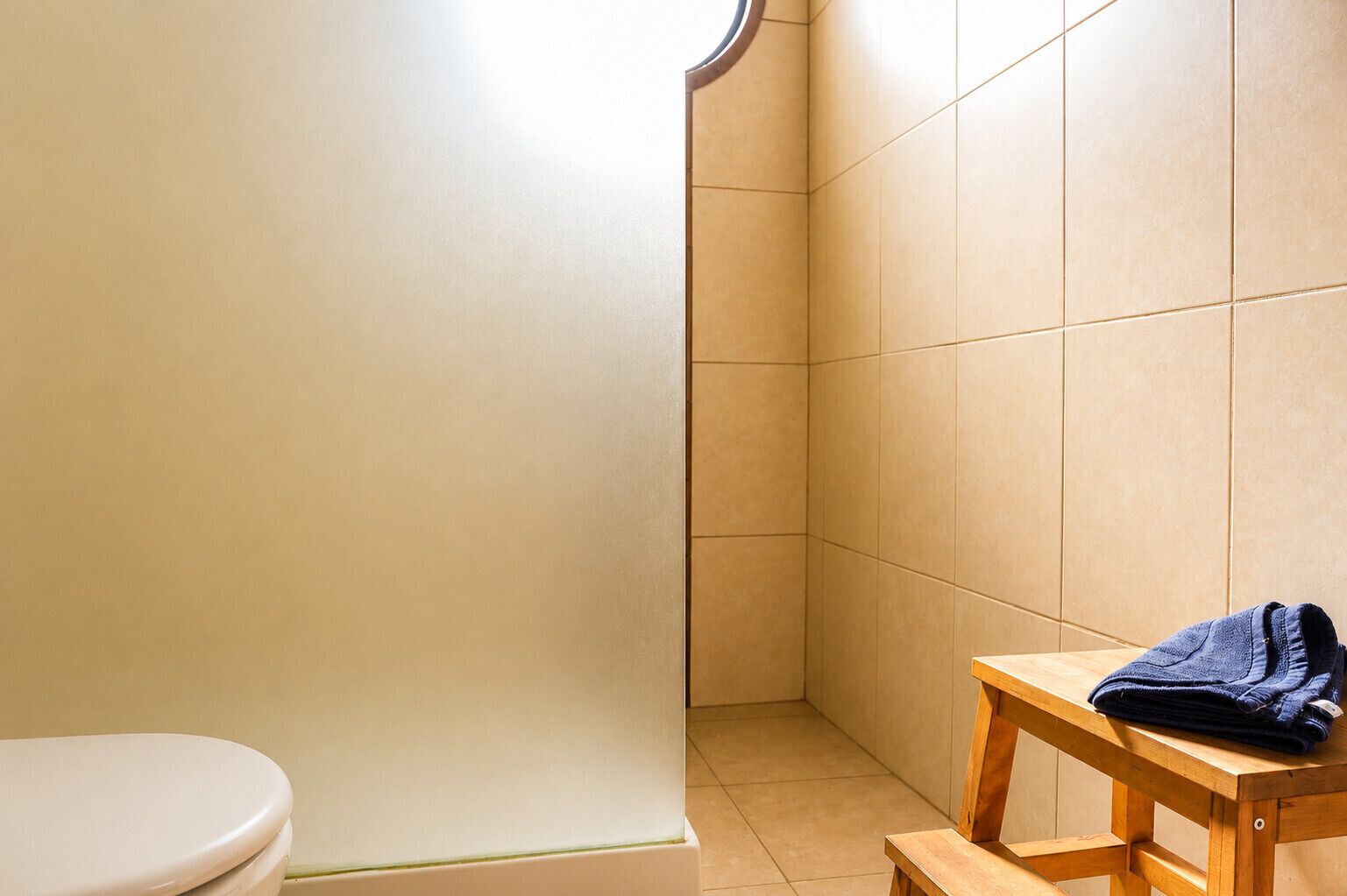 Un baño con inodoro, zona de ducha y un banco de madera con toalla.