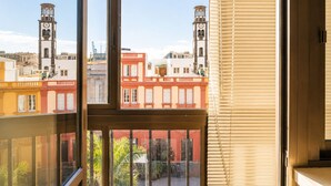A window with a view of buildings, including a clock tower, through a window with blinds.